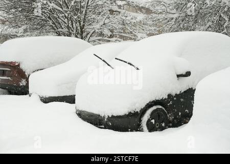 Multiple cars completely buried under thick snow in a parking lot after a heavy winter storm, with windshield wipers raised to prevent freezing. Stock Photo