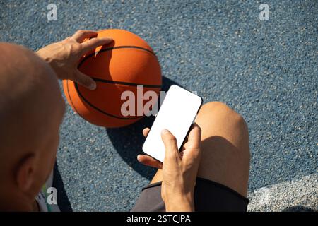 Basketball player using smartphone and texting social media during game interval, Outdoor training. View from above. Close up. Stock Photo