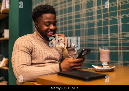 Freelancer is having pause from work, he is talking on smartphone and drinking hot chocolate in bar. Stock Photo