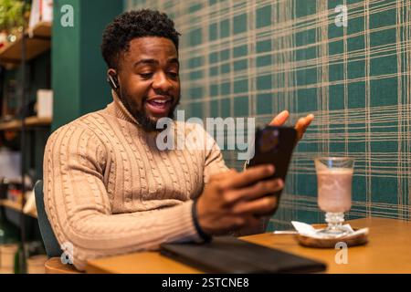 Freelancer is having pause from work, he is talking on smartphone and drinking hot chocolate in bar. Stock Photo
