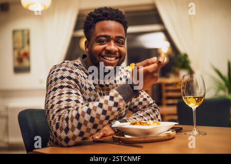Happy young black man is having dinner and wine at restaurant. He is looking at camera and smiling. Stock Photo