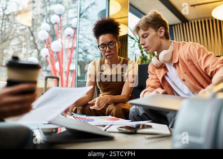 Two colleagues engage in a focused discussion, analyzing charts and documents at a hotel. Stock Photo
