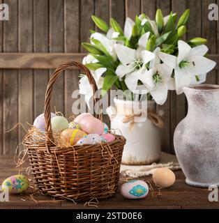 Colorful easter eggs in a basket and white lilies on a wooden table and background Stock Photo