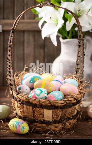Colorful easter eggs in a basket and white lilies on a wooden table and background Stock Photo