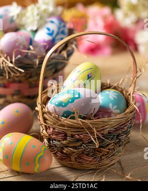 Decorated Easter eggs in a basket with flowers in background on a wooden table Stock Photo