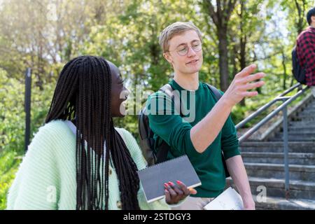 Two university students engaged in a conversation while taking notes in a natural setting. A great concept for learning, teamwork, and outdoor educati Stock Photo