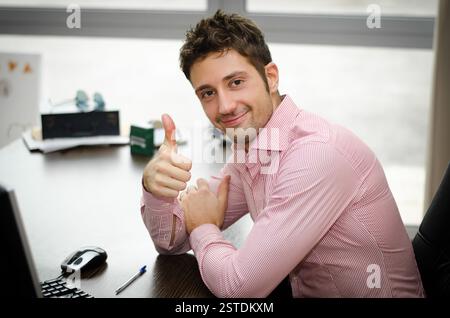 Cheerful office worker at desk doing thumb up sign and smiling Stock Photo