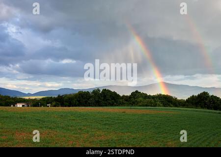 Rural landscape with field in the rain. With two rainbows in the blue sky. Chocholna, Slovakia Stock Photo
