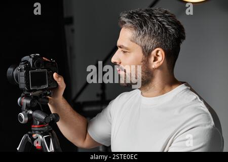 A man concentrates on adjusting his camera settings while standing in a modern studio. Stock Photo