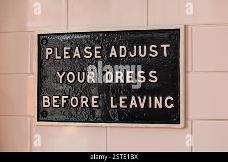 An old cast iron sign in a gents public toilet saying "Please adjust your dress before leaving", England, UK Stock Photo