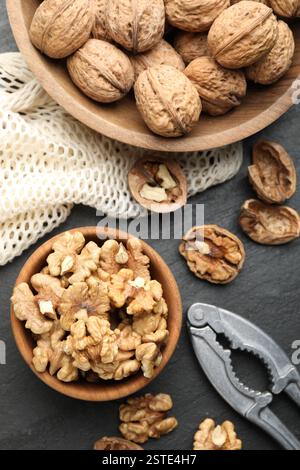 Fresh ripe walnuts, nutcracker and shells on black table, flat lay Stock Photo