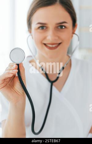 Using stethoscope. Young nurse is standing is in the office. Stock Photo