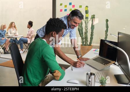 Side view high angle of smiling multiracial male colleagues talking about project at table in modern workspace Stock Photo