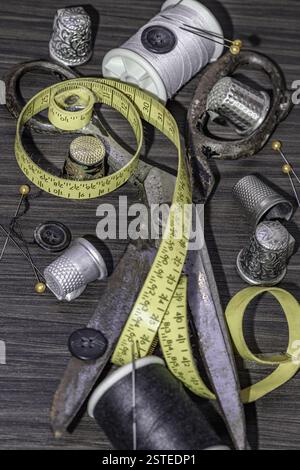Silver sewing needles, Thimbles, Steel scissors, Measuring tape, Black buttons, Spools of black and white thread including pins on wooden blackground. Stock Photo