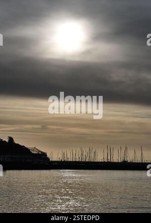 Sun penetrating through early morning hazy clouds over the masts of boats in the marina at Torquay, Devon, England. Stock Photo