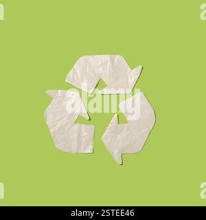 A crumpled white paper forming a recycling symbol is set against a solid green backdrop, embodying environmental responsibility. Stock Photo