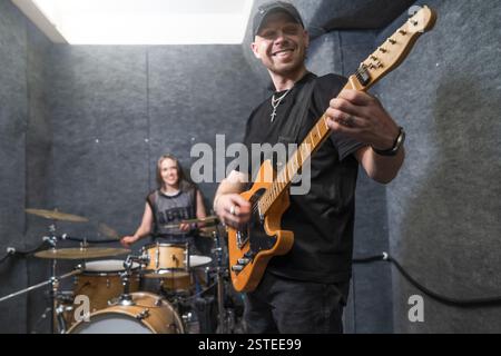Musicians performing rock music in soundproof studio. Guitarist playing electric guitar while female drummer plays drums, creating energetic atmosphere. Ideal for music, performance, band themes. Stock Photo
