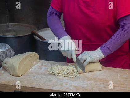 Hands are cutting dough on cutting board with knife. Kalguksu, traditional Korean knife-cut wheat flour noodles at Gwangjang Market, Seoul, Korea Stock Photo