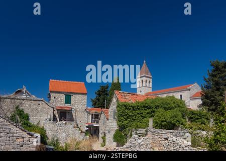 Idyllic rural scene showcasing a charming stone-built village featuring a church tower surrounded by greenery under a vivid blue sky. Stock Photo