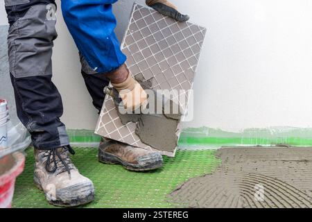 Bricklayer tiler spreads glue on new floor tiles with trowel. Construction industry. Building. Stock Photo