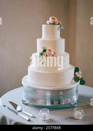 A stunning four-tier wedding cake with floral accents displayed elegantly at the event. Stock Photo