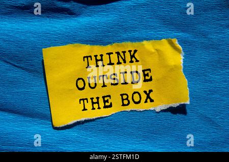 Think outside the box message written on ripped torn yellow paper on blue background. Conceptual think outside the box symbol. Copy space. Stock Photo
