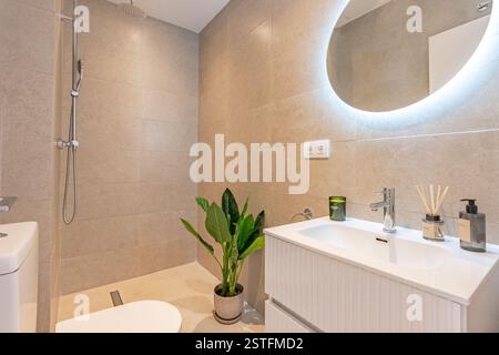 a close up image of a stone tile bathroom with illuminated mirror and standing shower in mediterranean holiday home Stock Photo