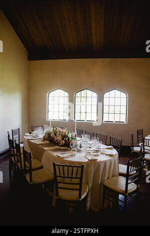 A beautifully arranged dining table set with glassware and flowers in a rustic venue with large windows. Stock Photo