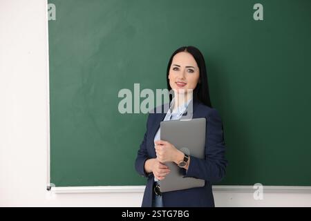 English teacher with laptop near chalkboard in classroom Stock Photo