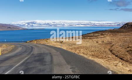 Winding tarmac road through the Westfjords in Iceland with snowcapped mountains and sea view in the background. Stock Photo