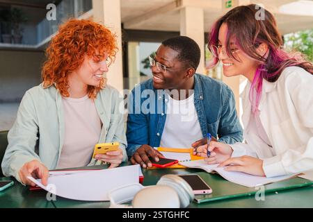 Three enthusiastic students collaborating together on academic projects while sharing ideas and discussing important concepts during their study session at a university campus in a friendly meeting. High quality photo Stock Photo