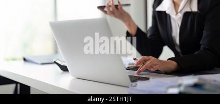 Multitasking financial professional on a call while managing data and calculations in a modern office. Stock Photo