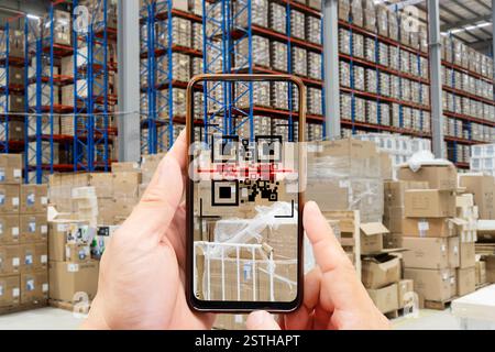 Person scanning QR code on smartphone in a warehouse with stacked boxes. Inventory management, supply chain logistics, warehouse automation, barcode s Stock Photo