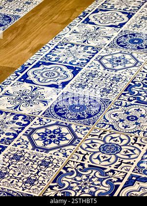 Blue and White Ceramic Tiles with Decorative Patterns  Close-up of ceramic tiles with intricate blue and white patterns, alternating with wooden plank Stock Photo