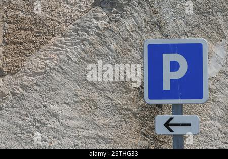 A blue car park sign with a white arrow on a rough, textured wall, France, Europe Stock Photo