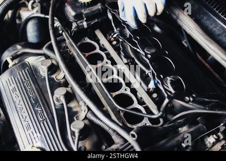 Mechanic working on a car engine with components and cables visible, wearing gloves Stock Photo
