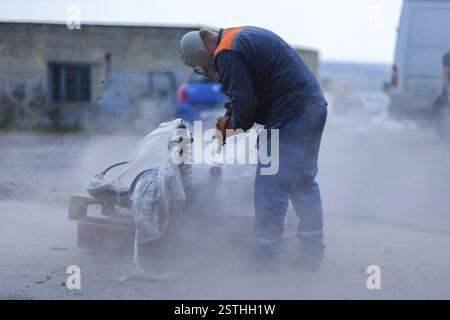 Man wearing protective gear sanding outside, surrounded by dust Stock Photo