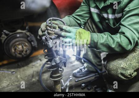 Mechanic in green uniform assembling coil springs with tools in a dimly lit workshop Stock Photo