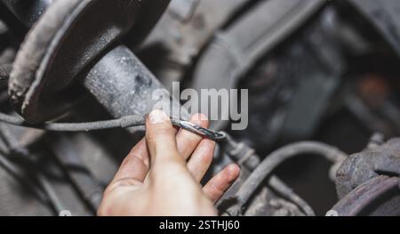 Hand holding a wire in a car's mechanical setting, depicting automotive repair Stock Photo