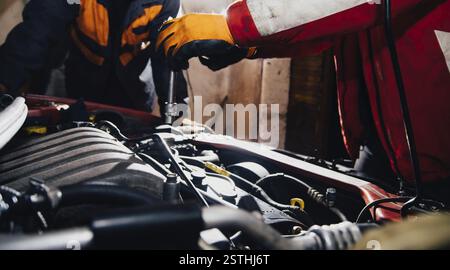 Mechanic wearing gloves works on a car engine in a dimly lit garage setting Stock Photo