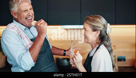 Singing, cooking and couple together in kitchen for karaoke, retirement celebration or excited for love in home. Senior man, woman or song for music Stock Photo
