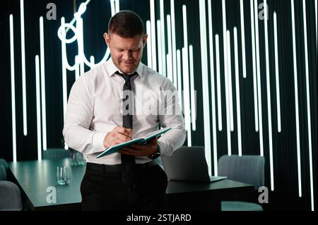 Meeting Room. The manager is preparing for the meeting. A young man in a white shirt is taking notes in a notebook before an important meeting. Stock Photo