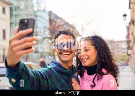 Young happy couple enjoying a city adventure, capturing a joyful selfie with their smartphone while exploring during vacation Stock Photo
