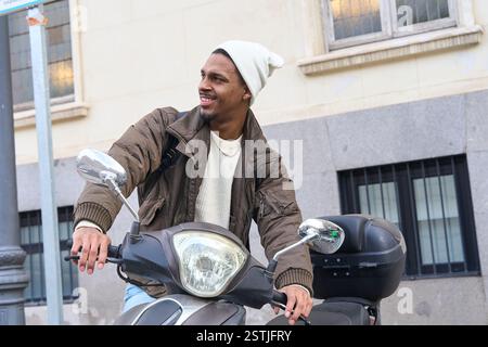 Happy delivery man riding a scooter through the city, dressed in warm winter clothes and enjoying his day while commuting Stock Photo