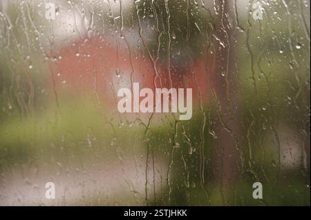Rain running down window glass. Green and red blurry background. Stock Photo