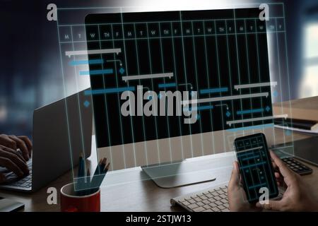 PROJECT MANAGEMENT businessman using a cell phone and laptop to view a project plan Management Software. Scene is focused and professional. Stock Photo