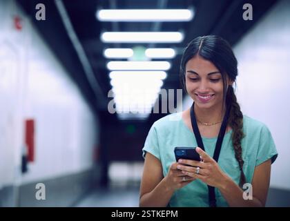 Smiling female technician looking at smart phone in server room Stock Photo
