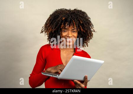 Young woman with curly hair smiles while using her laptop, embracing modern technology and connectivity Stock Photo
