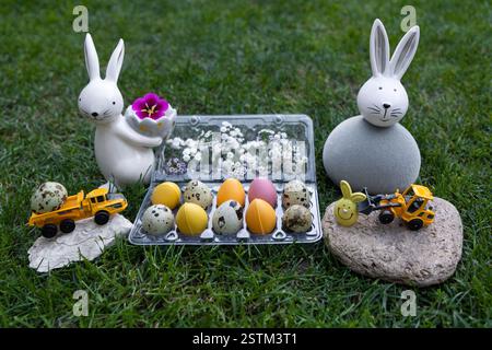 Two toy models of excavator and dump truck near bright multi-colored Easter eggs and souvenir rabbits. Stock Photo