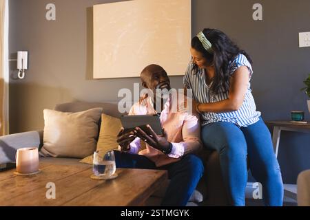 Senior diverse couple enjoying time together at home, using tablet on cozy sofa. Technology, lifestyle, mature, relaxing, leisure, elderly Stock Photo
